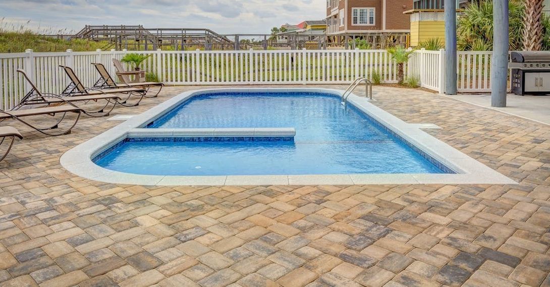 A large swimming pool surrounded by chairs and a brick patio.