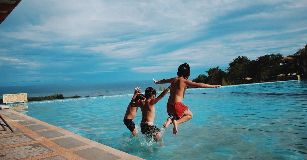 Three children are jumping into a swimming pool.