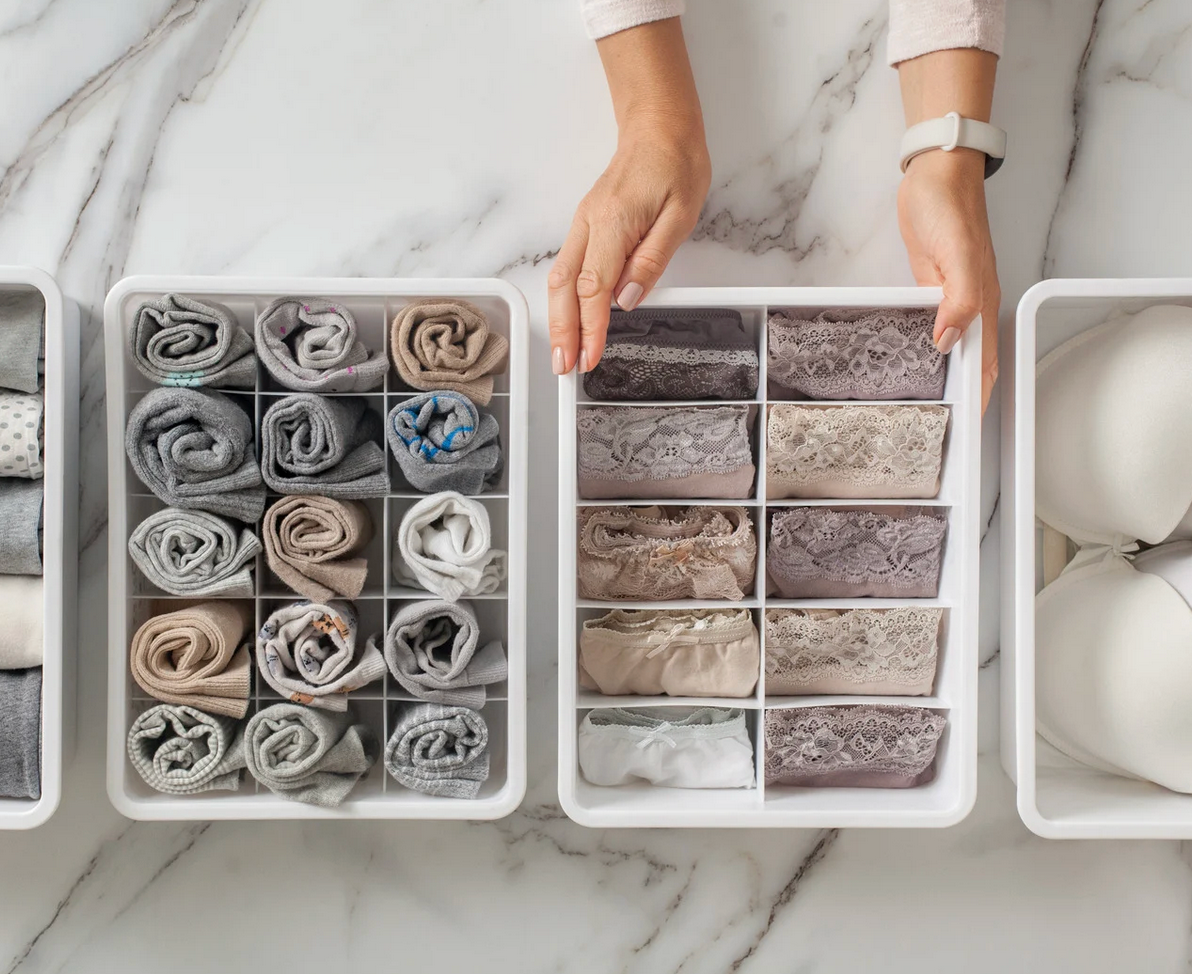 A woman is organizing her underwear in boxes on a marble counter.