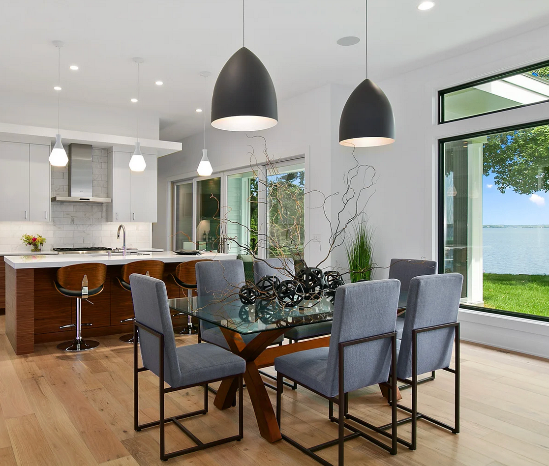 A dining room with a glass table and chairs and a view of the water.