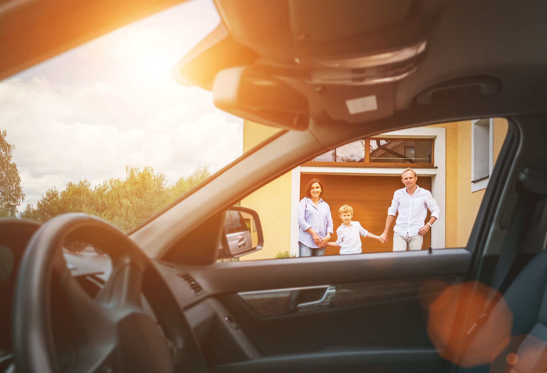 A family is standing in front of a garage in a car holding hands.