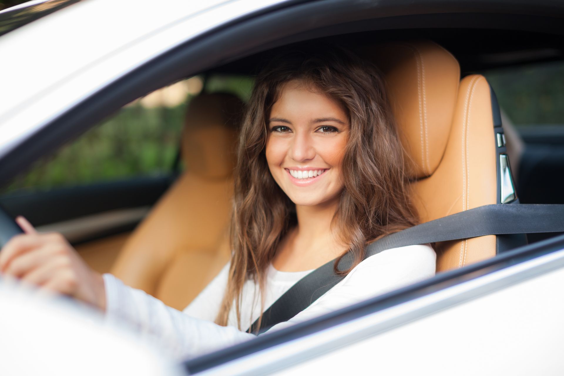 A woman is sitting in the driver 's seat of a car and smiling.