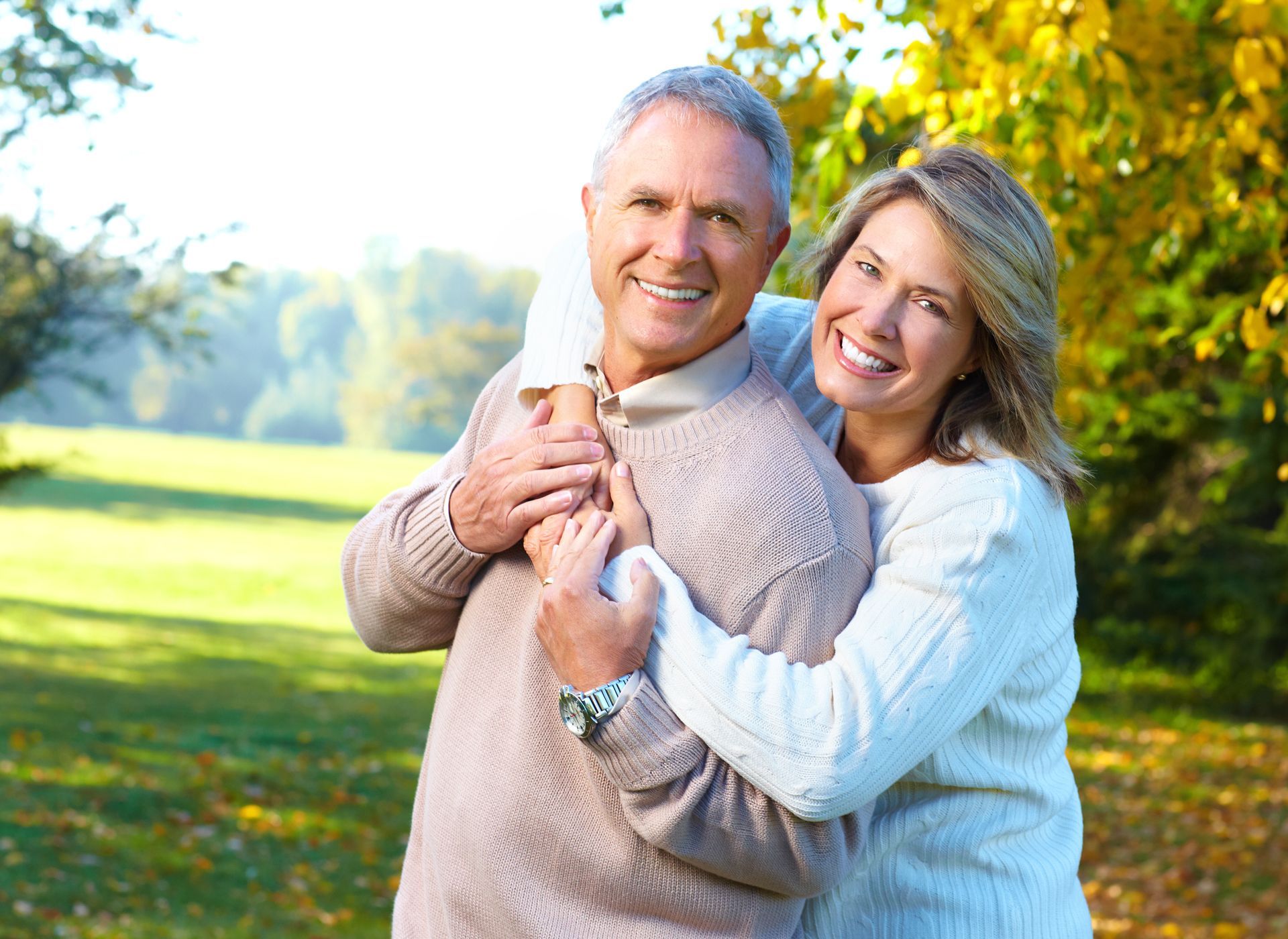 A man and a woman are hugging each other in a park.
