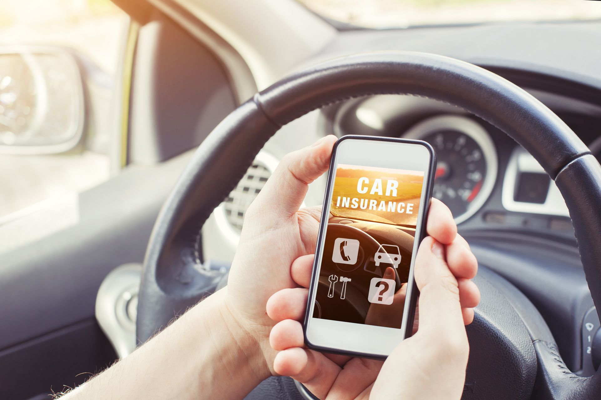 A person is holding a cell phone in their hand while driving a car.