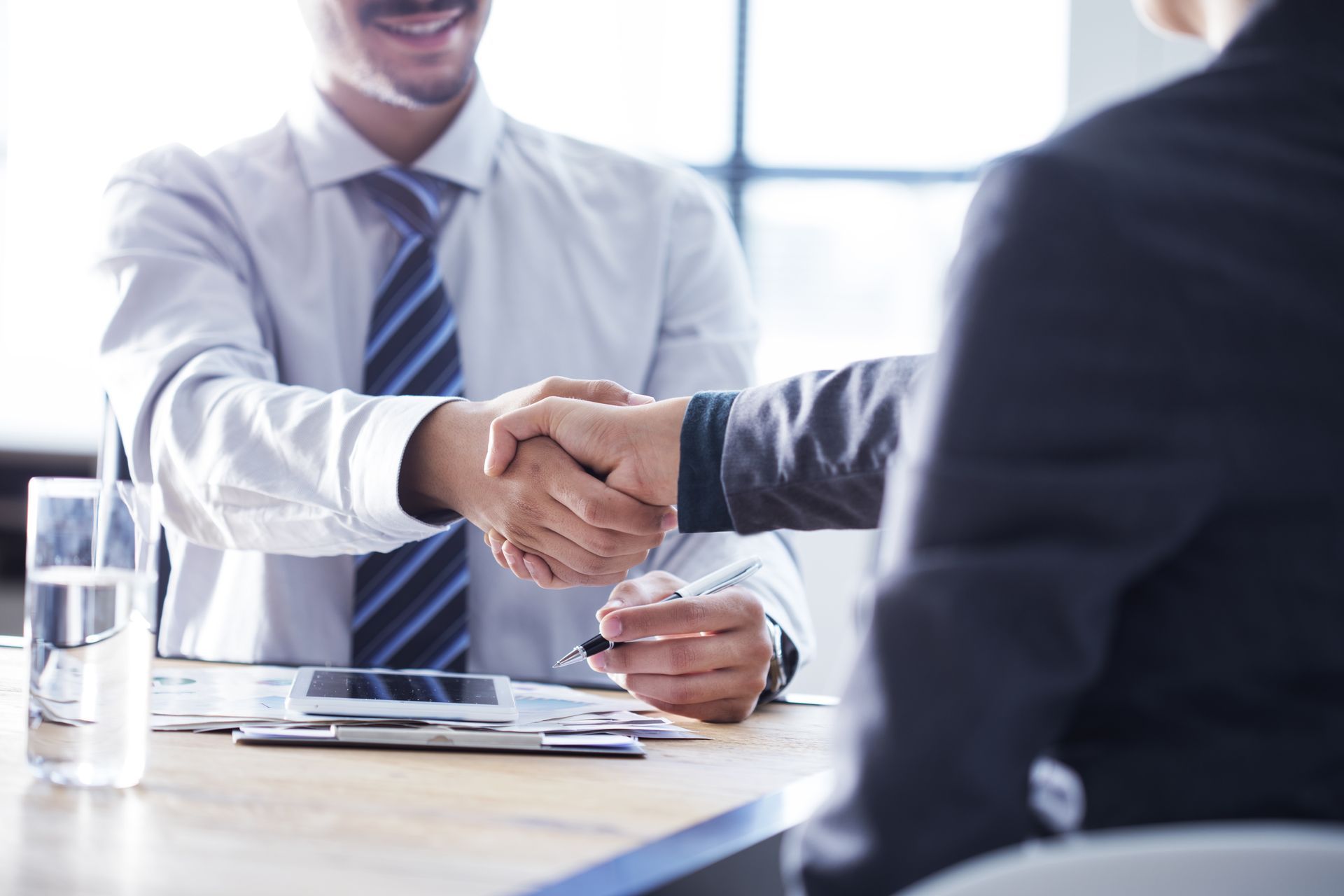A man and a woman are shaking hands at a table.