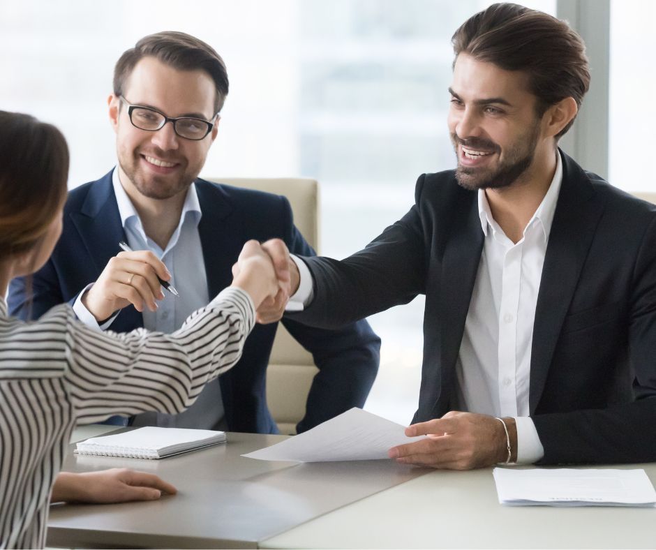 A man and a woman are shaking hands while sitting at a table.