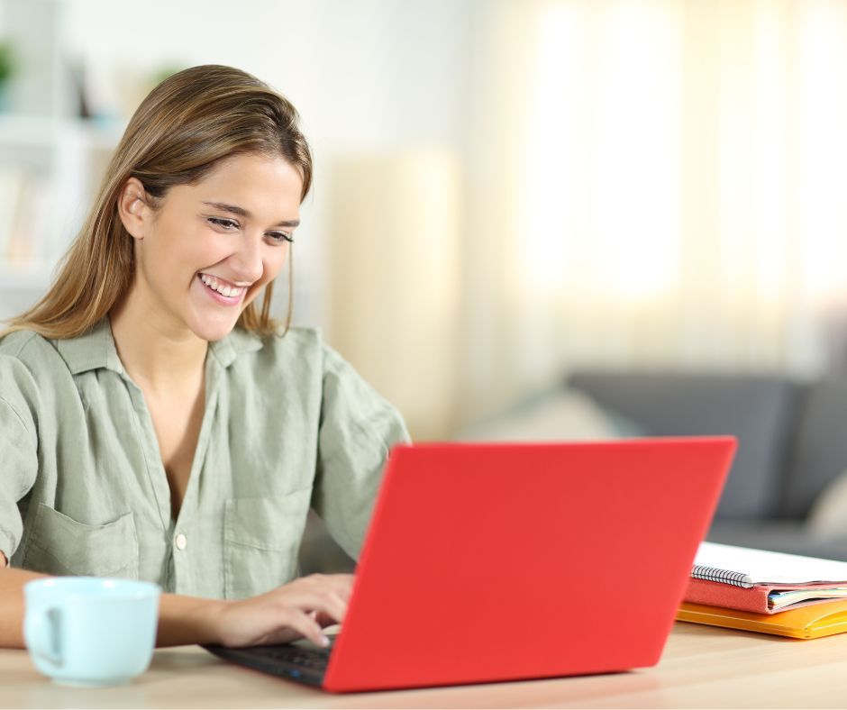 A woman is smiling while using a red laptop computer.