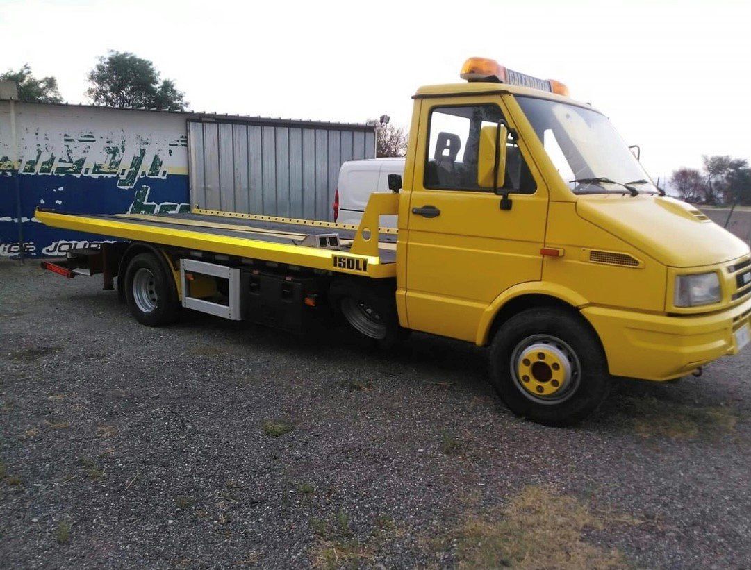 Un carro attrezzi giallo è parcheggiato in un parcheggio ghiaioso