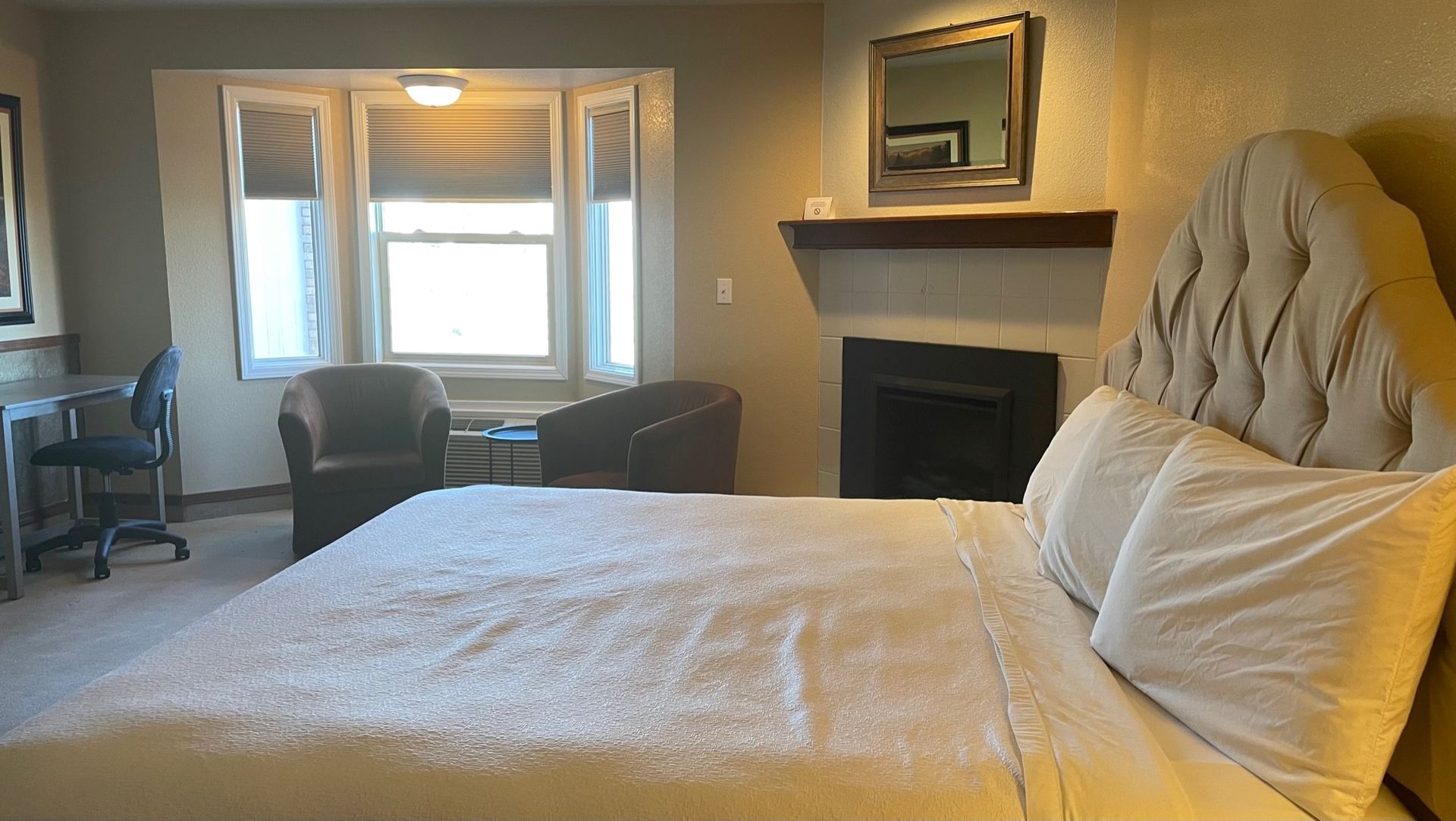 A hotel room with a king size bed , fireplace , chairs and a desk.