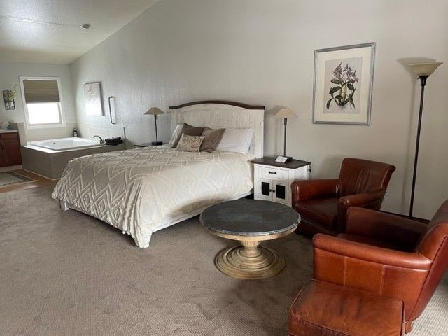 A bedroom with a bed , chairs , table and jacuzzi tub.