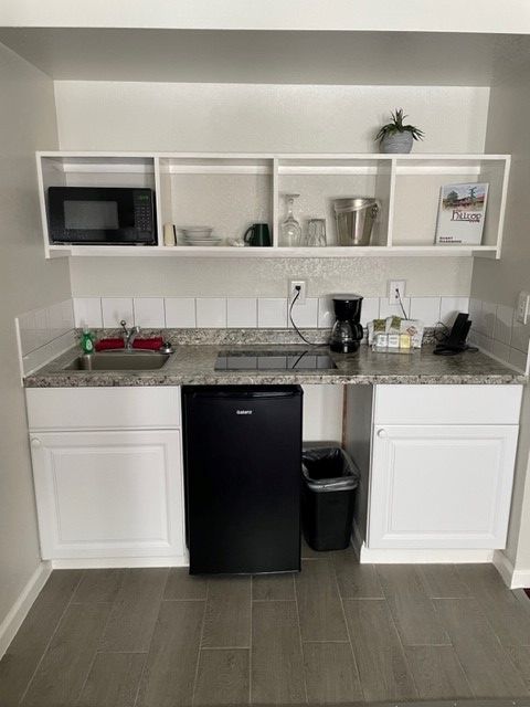 A small kitchen with white cabinets , a black refrigerator , a sink , and a microwave.