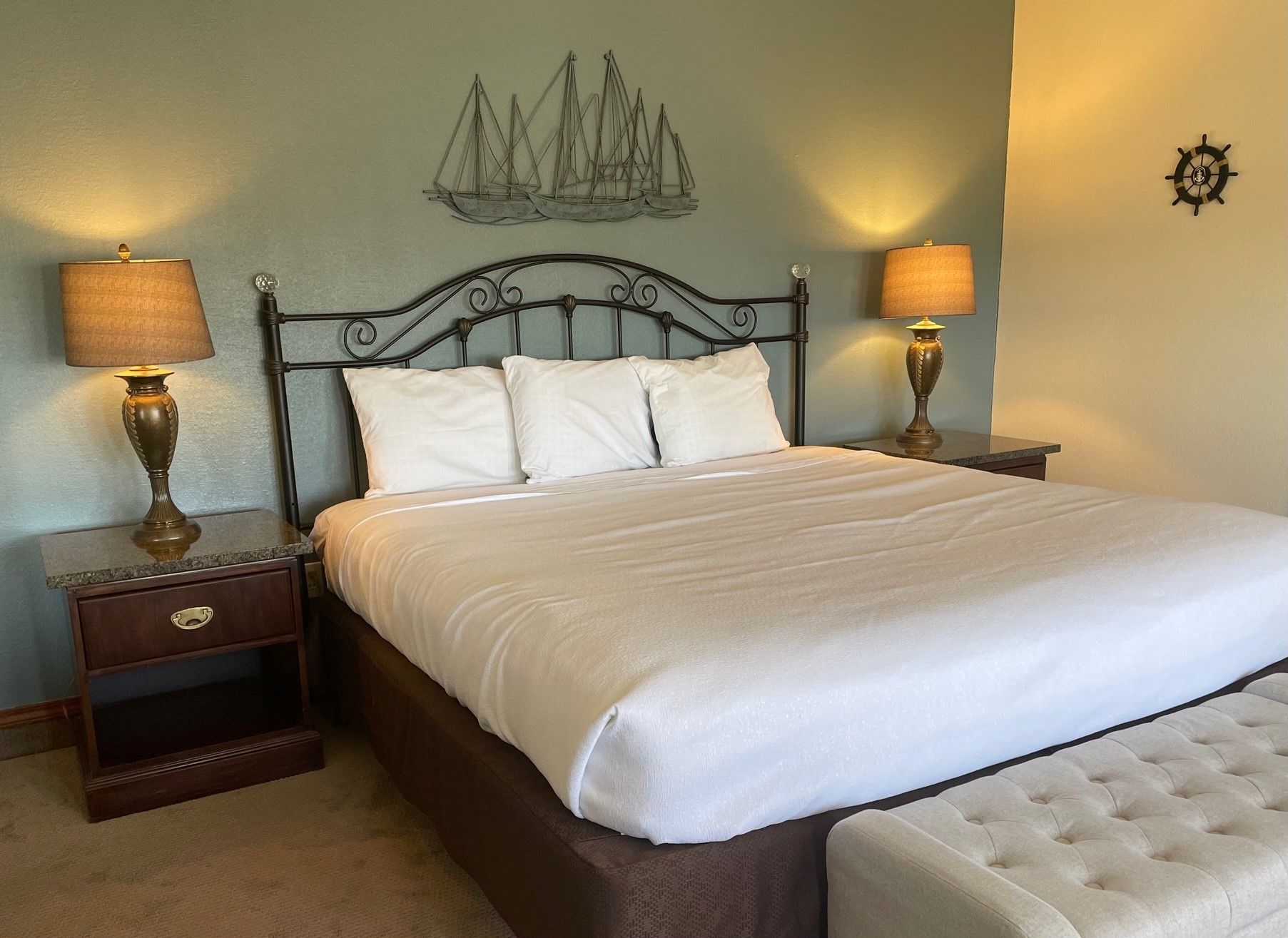 A bedroom with a king size bed , two nightstands , two lamps and a steering wheel on the wall.