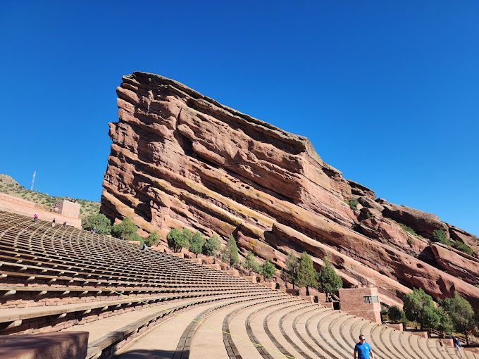 A man is standing in front of a large rock formation in an amphitheater.