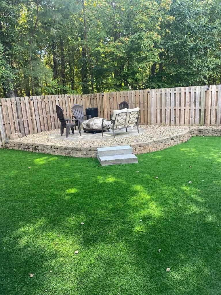 A backyard with a fire pit , chairs , and a wooden fence.