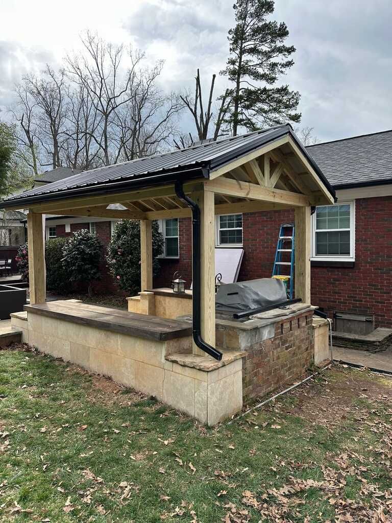 A wooden gazebo is sitting in front of a brick house.