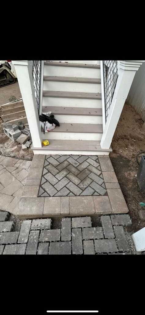 A cat is sitting on the sidewalk next to a set of stairs.