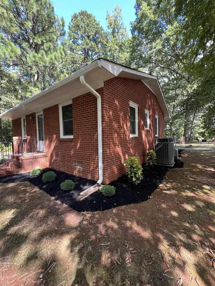 A red brick house with a white roof is surrounded by trees.