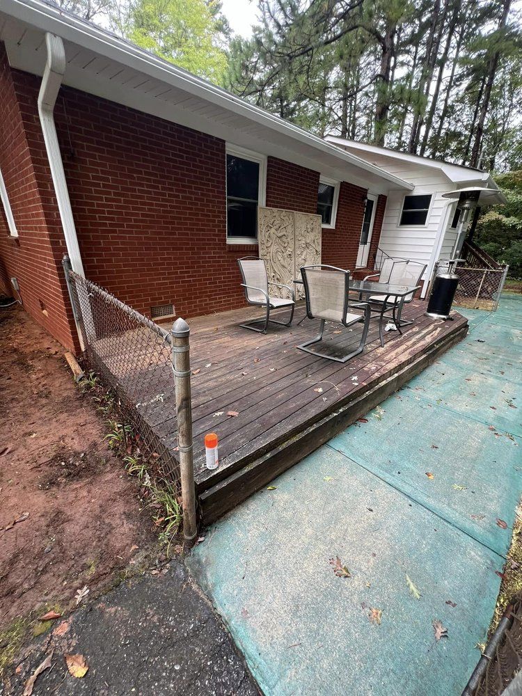 There is a deck with a table and chairs on it in front of a brick house.