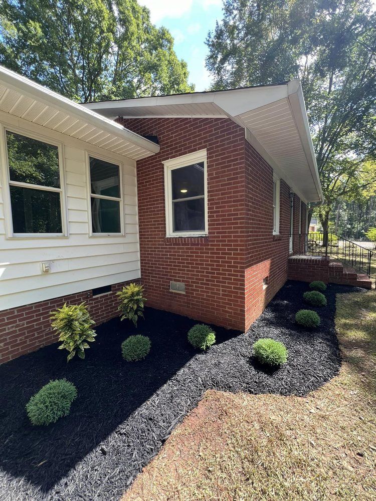 A brick house with a white siding and black mulch in front of it.