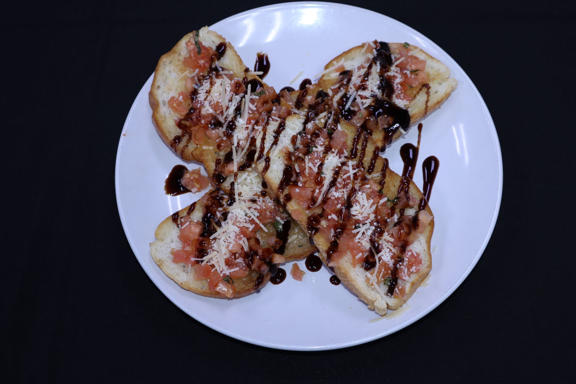Toasted bread topped with tomato, cheese, and balsamic glaze on a white plate.