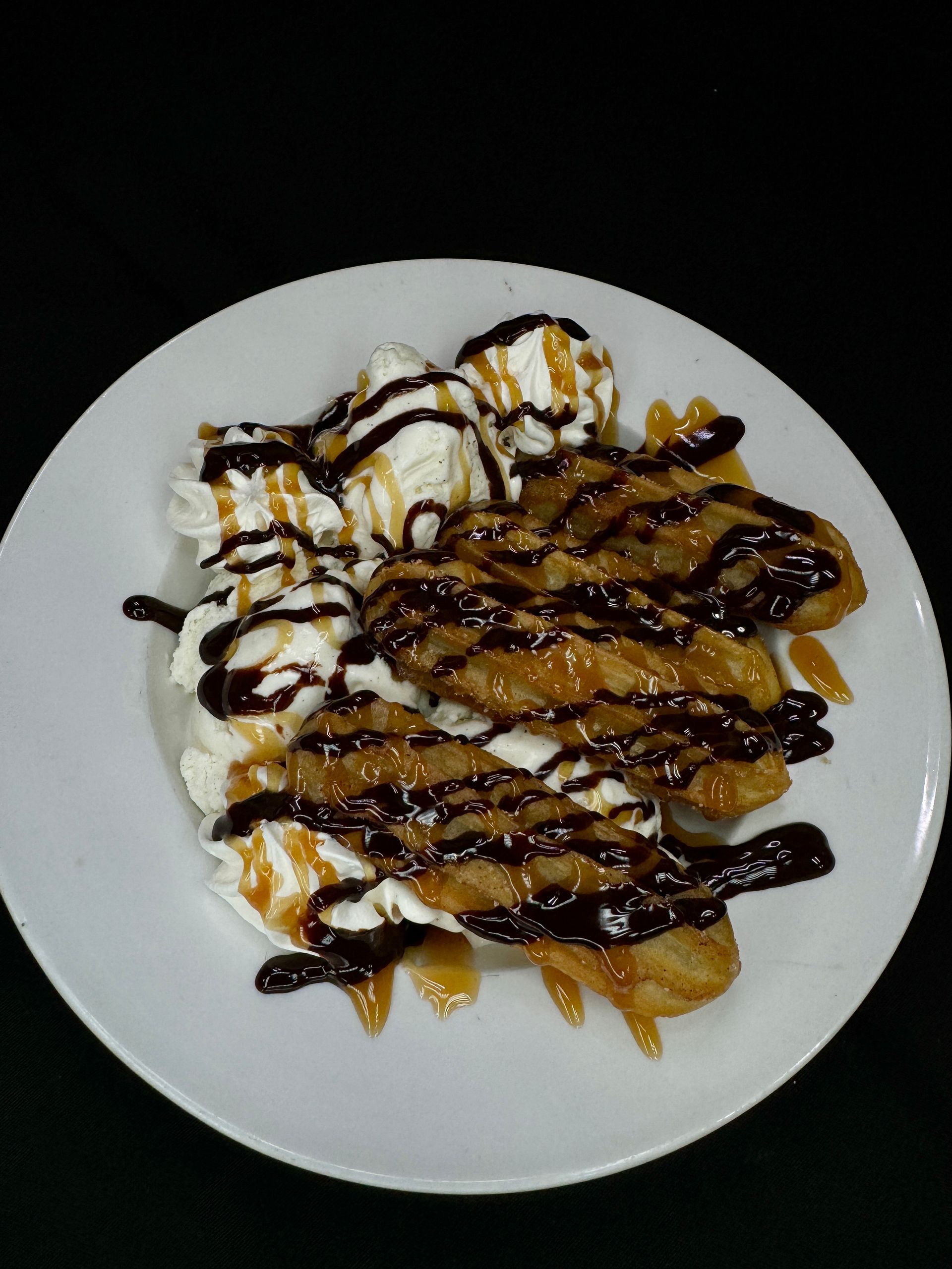 Fried bananas with ice cream, caramel, and chocolate sauce on a white plate.