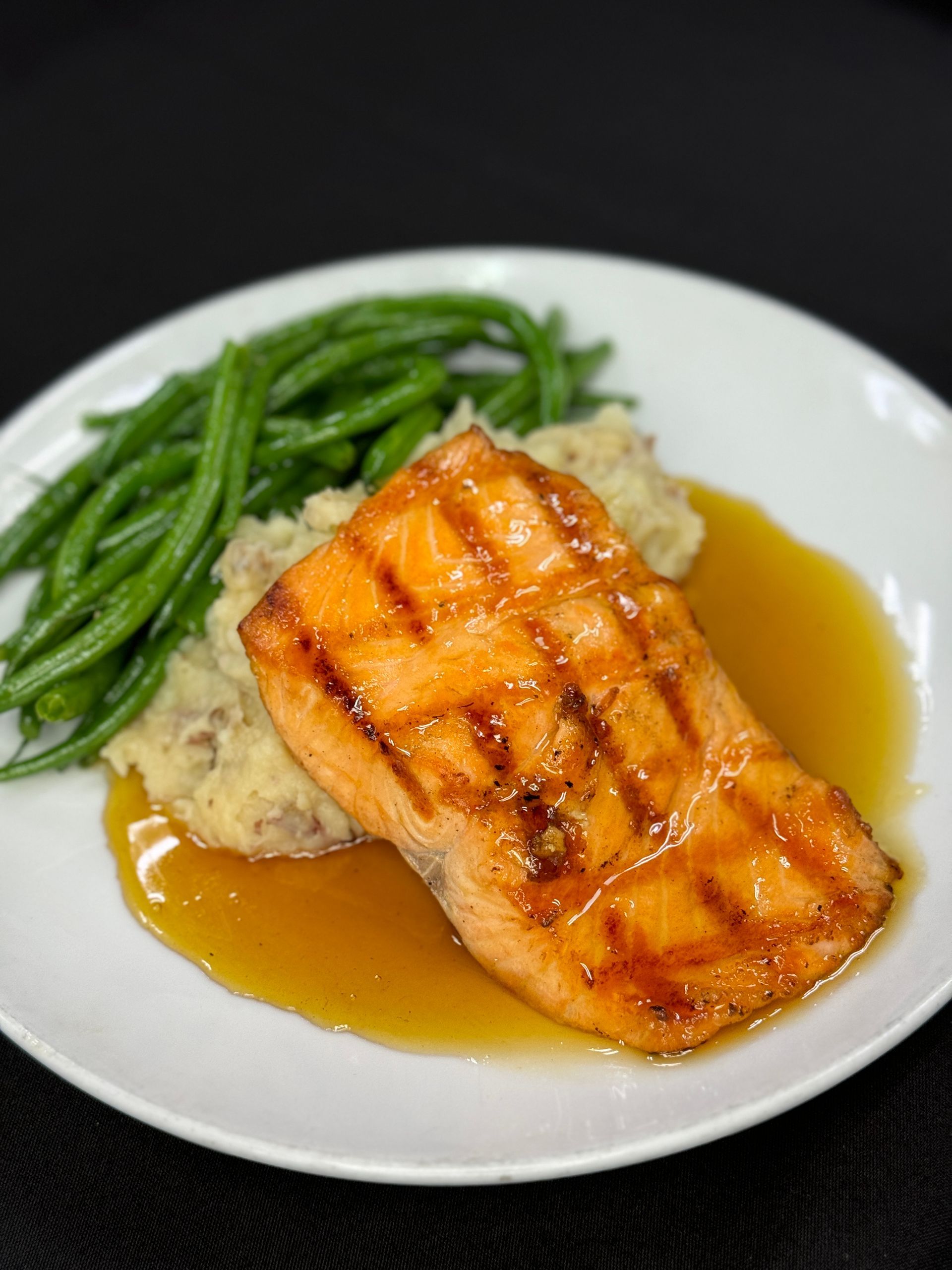 Grilled salmon with mashed potatoes and green beans on a white plate.