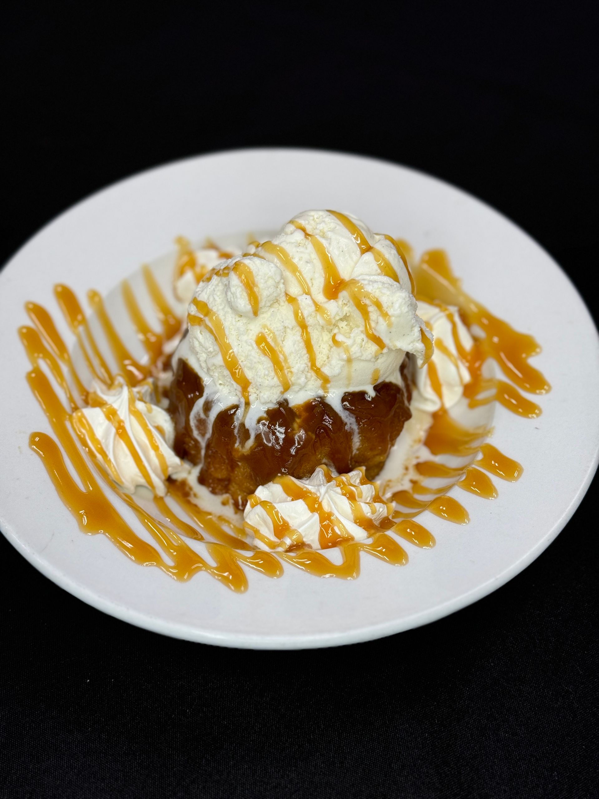 Dessert: Warm apple cake topped with ice cream, whipped cream, and caramel sauce on a white plate.
