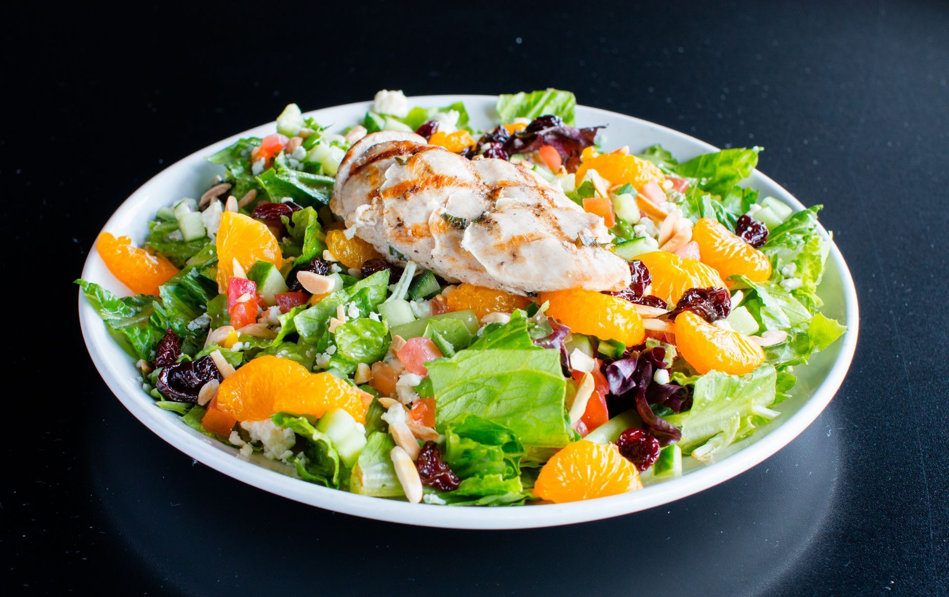 A white plate topped with a salad with chicken and oranges.