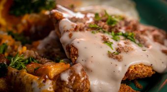 Fried chicken smothered in white gravy, garnished with parsley. Includes potatoes.