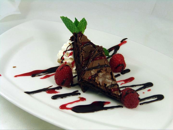 A brownie with raspberries and whipped cream on a white plate.