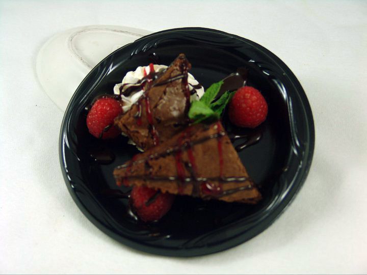 A slice of chocolate cake with whipped cream and strawberries on a black plate.