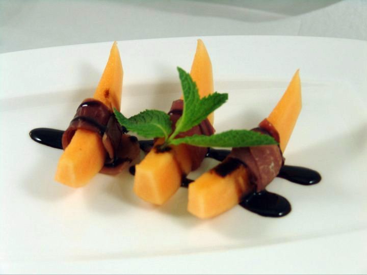 A white plate topped with carrots wrapped in bacon and mint leaves.