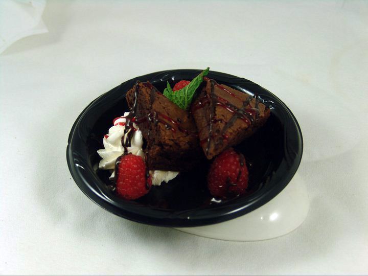 A bowl of brownies with whipped cream and raspberries.