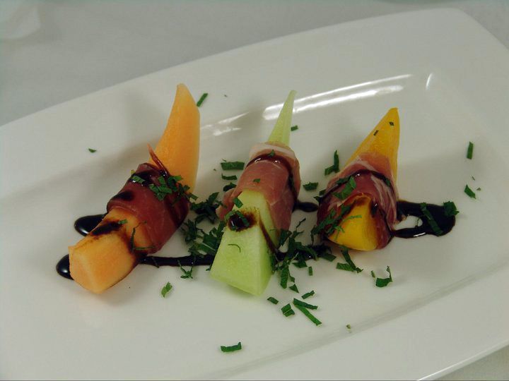 A white plate topped with slices of melon and ham.