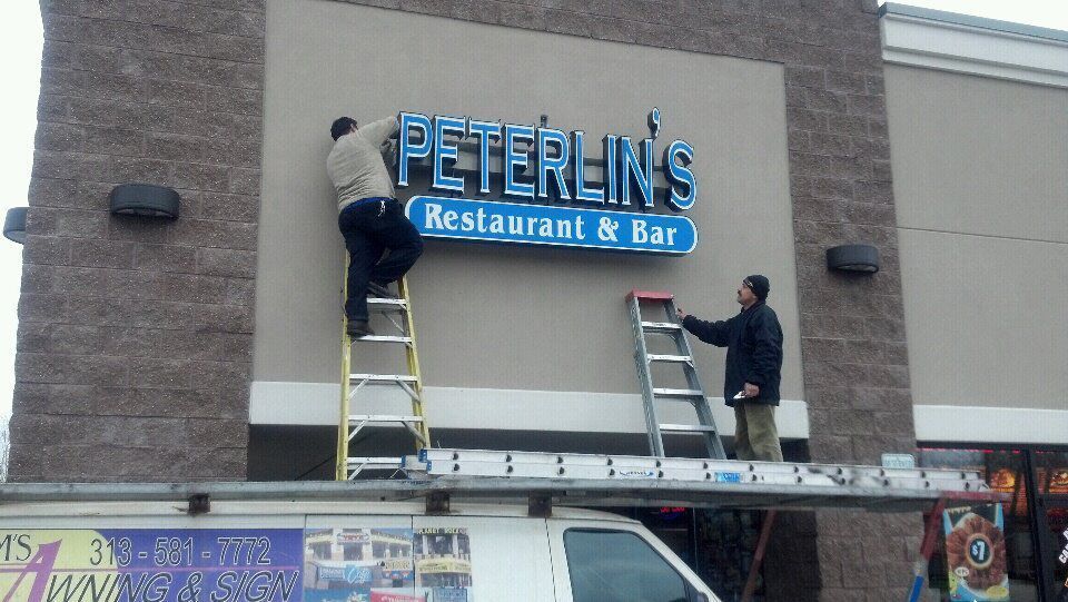 Two men are working on a sign for peterlin 's restaurant and bar.