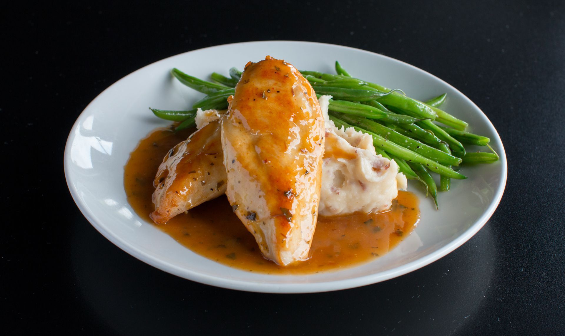 A white plate topped with chicken , mashed potatoes and green beans.