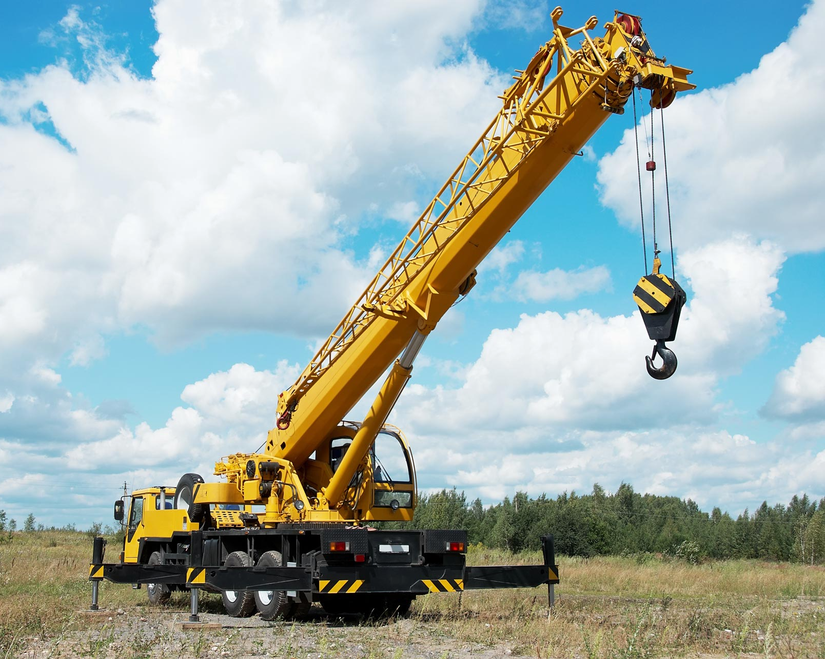 A large yellow crane is sitting in the middle of a field.