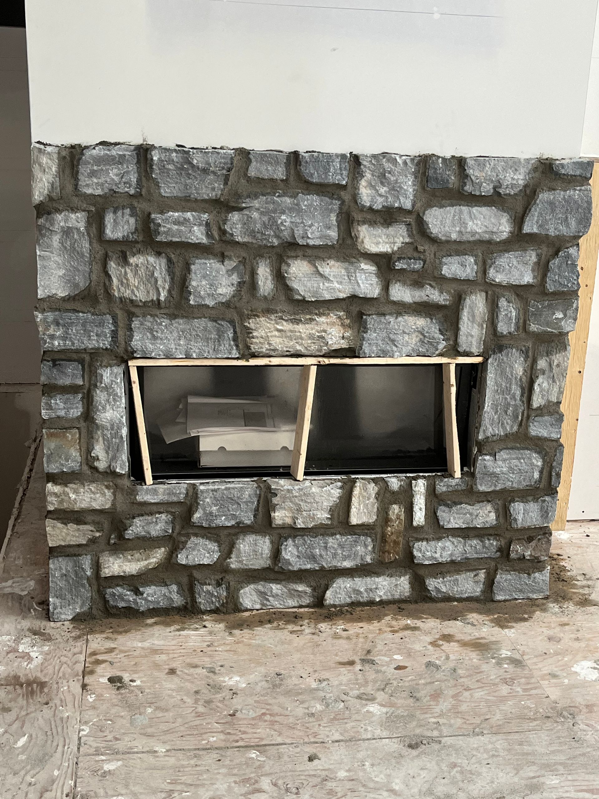 Une cheminée en pierre est en cours d'aménagement dans une pièce.
