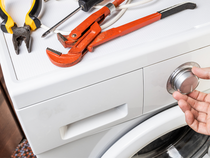 A person turning a knob on a white washing machine. Tools lie on top.