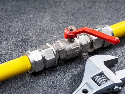 Yellow gas pipe with valve, wrench, on gray surface.