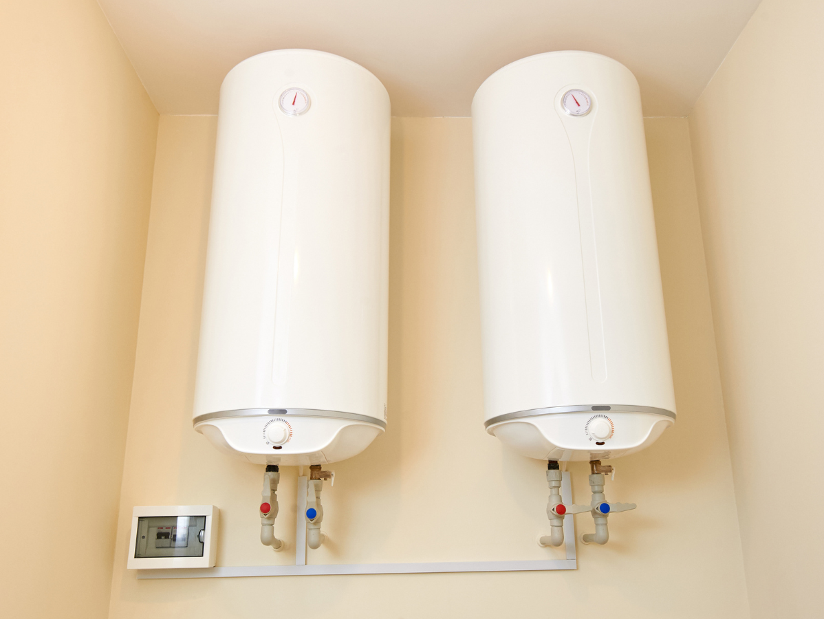 Two white water heaters mounted on a beige wall with connected plumbing.