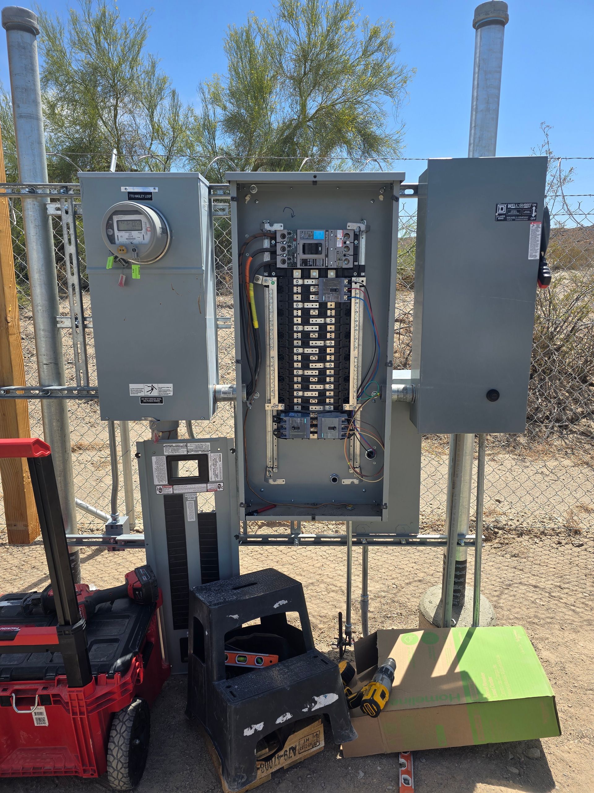 Electrical panel box with exposed circuits, tools, and a meter, outdoors.
