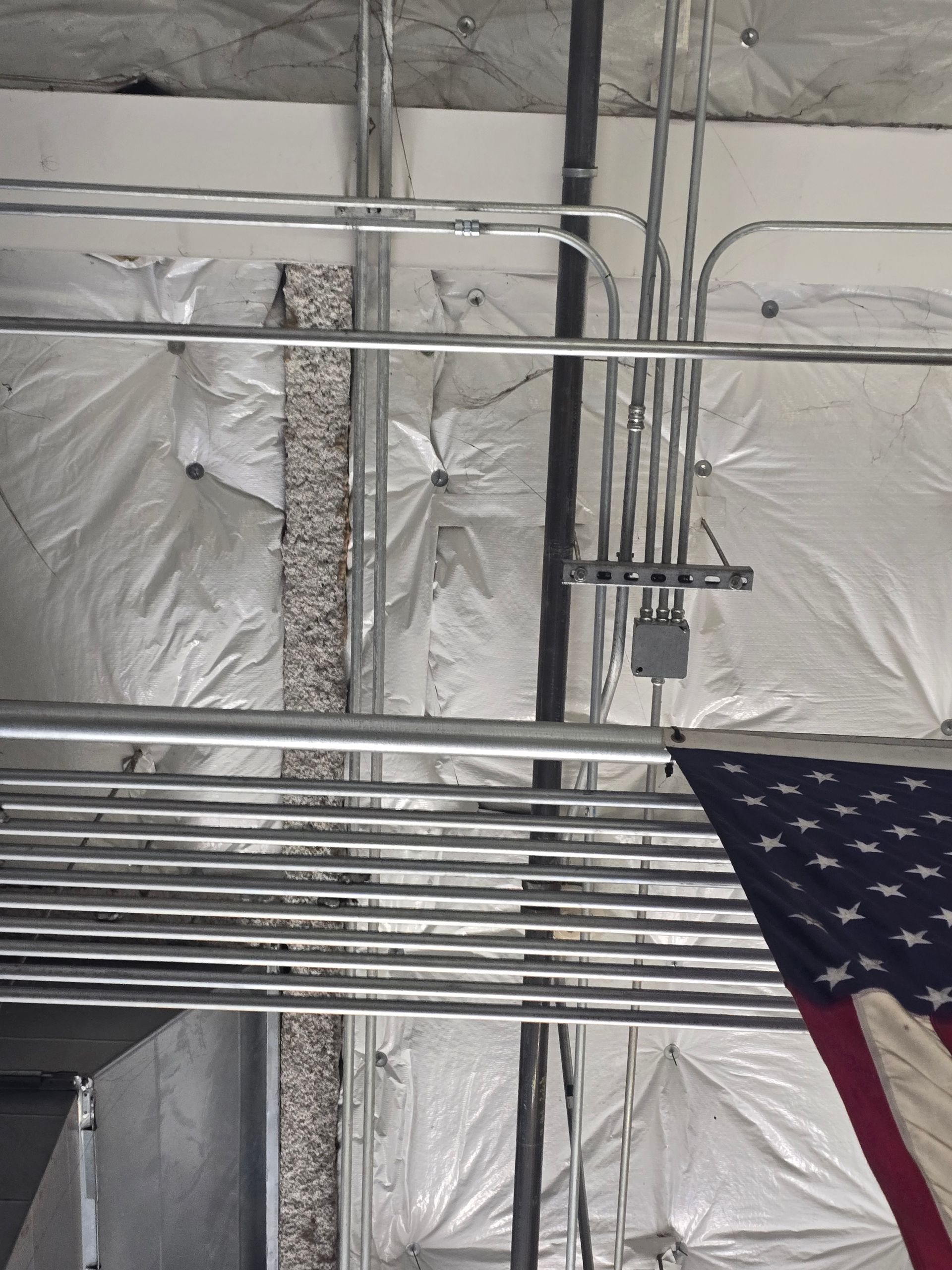 Electrical conduits and junction box installed on a ceiling with insulation, American flag partially visible.