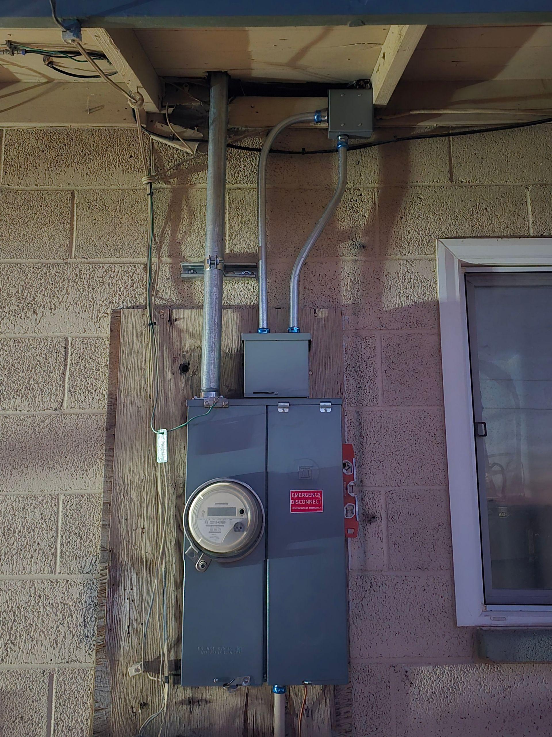 Electrical meter and panel on a concrete block wall, with conduits and a window visible.