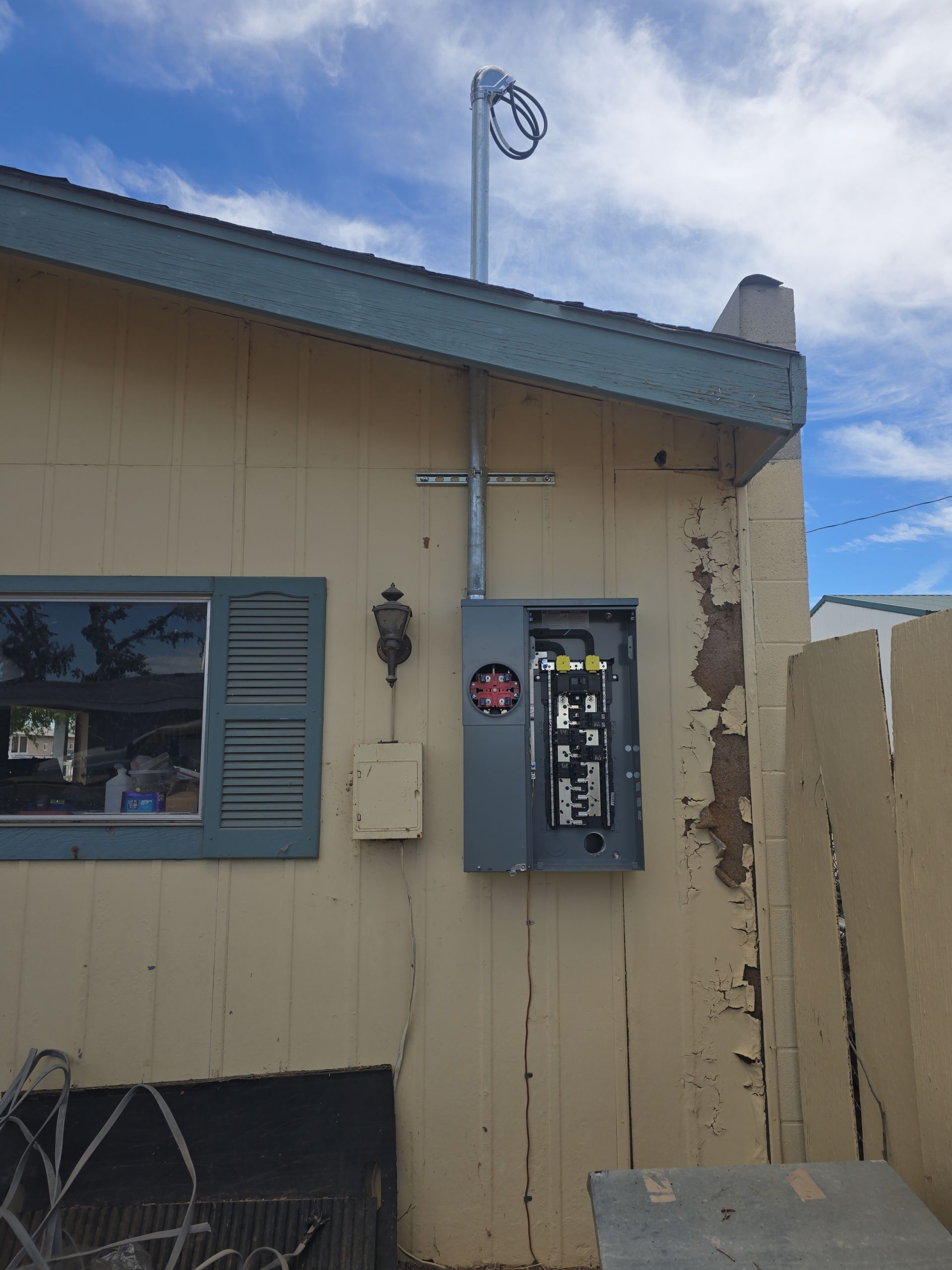 Exterior electrical panel mounted on a beige building with conduit to overhead service wires.