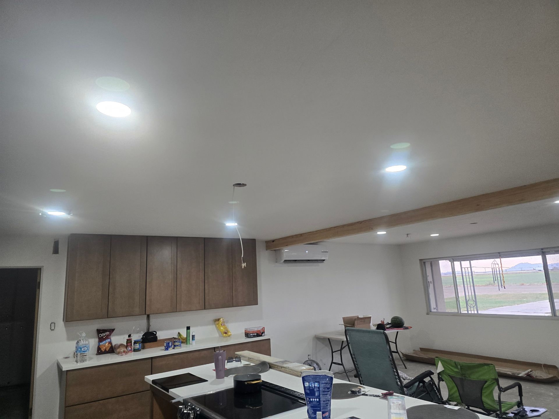 Kitchen interior: cabinets, island with stovetop, lights, windows with outdoor view.