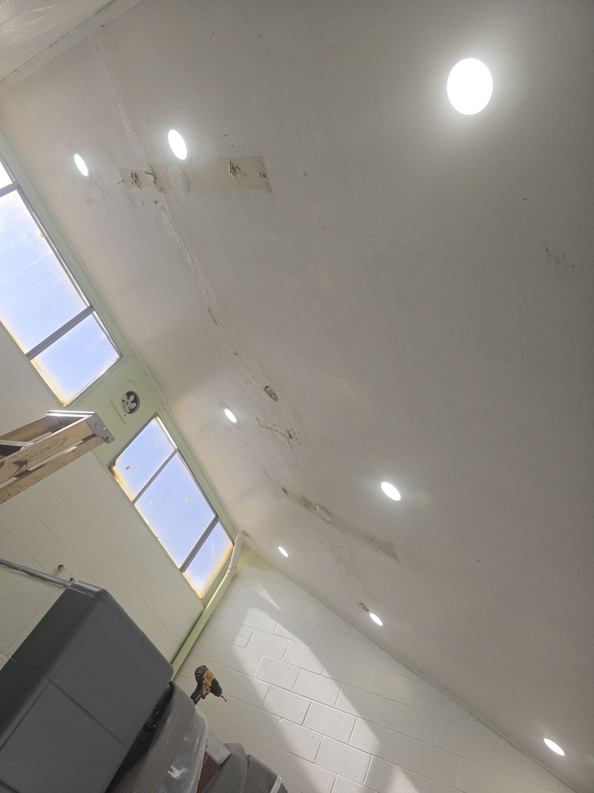 White room interior with recessed lights and two windows letting in sunlight.