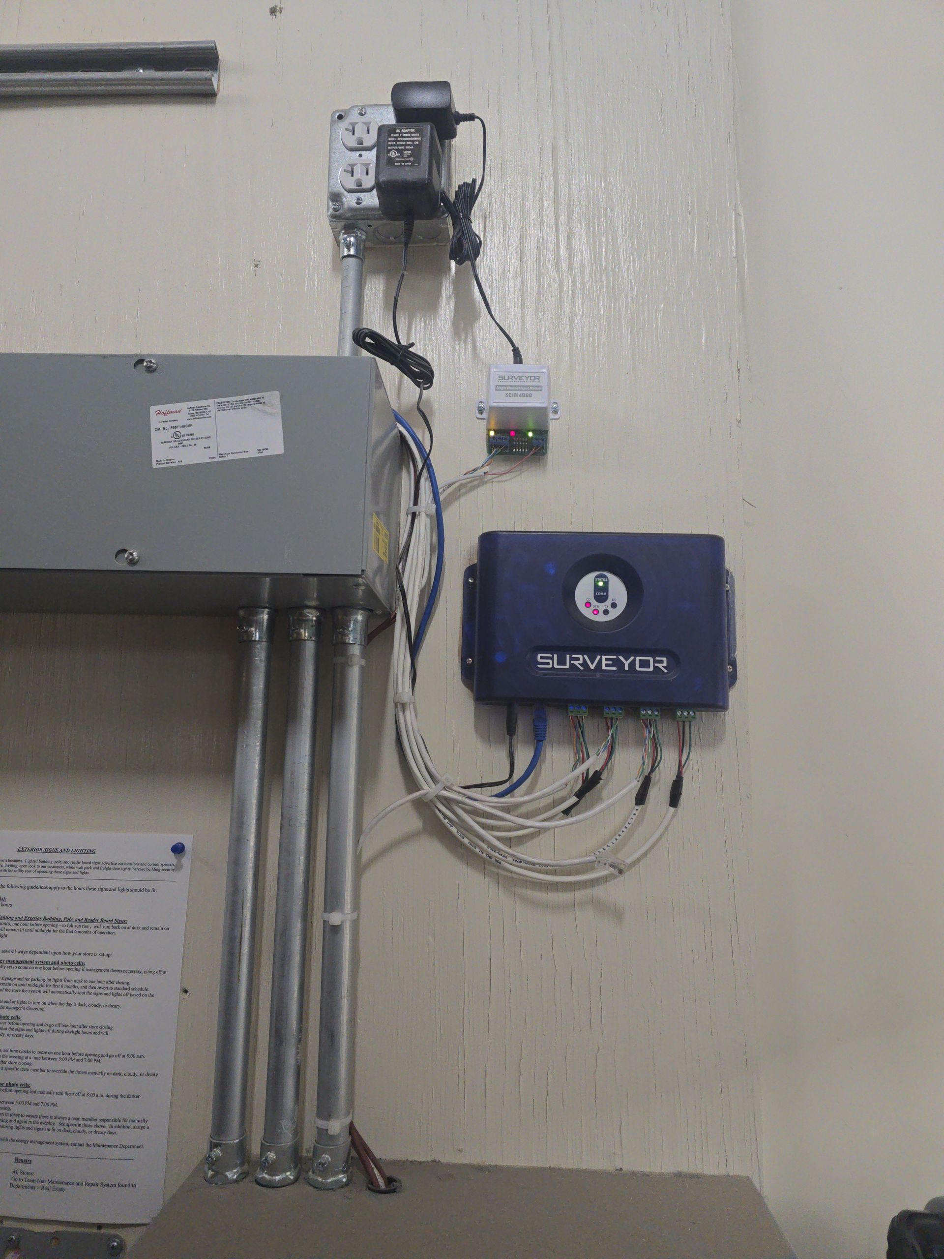 Electrical panel, wiring, and blue security system mounted on a beige wall.