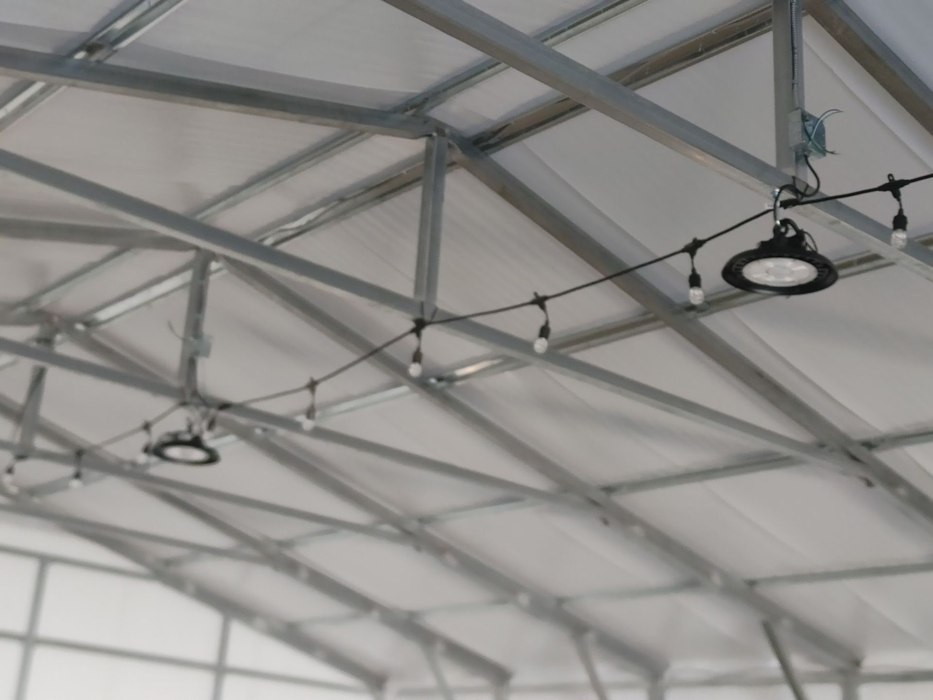 Metal tent frame with string lights and two black round lights hanging. White canvas roof.