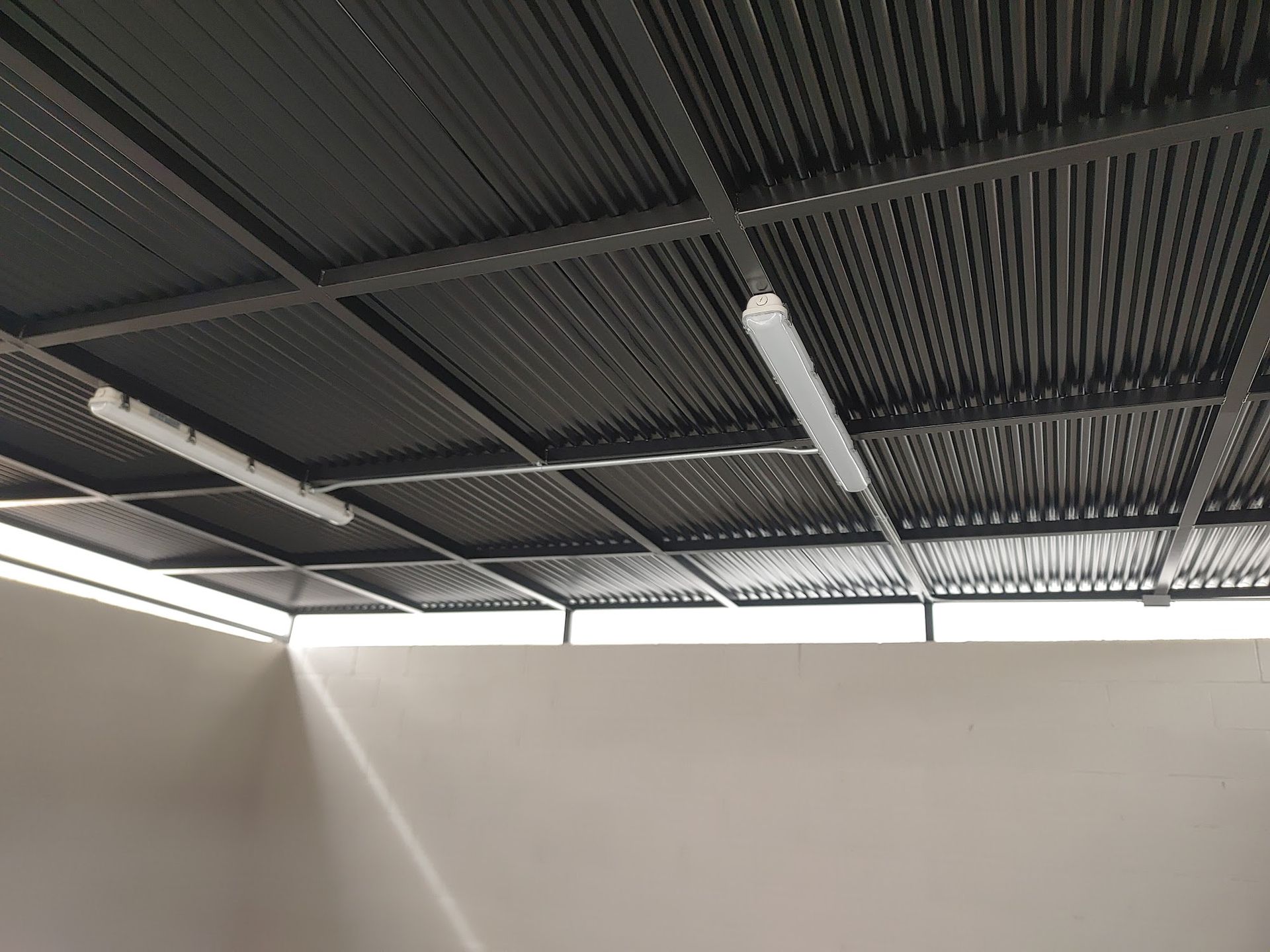 Dark corrugated metal ceiling with two fluorescent lights, indoors, looking up.